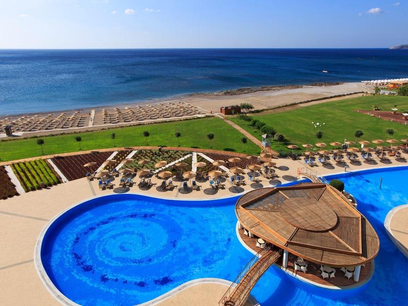 Piscina blu con bar sull'acqua, spiaggia e mare sullo sfondo sotto un cielo limpido.