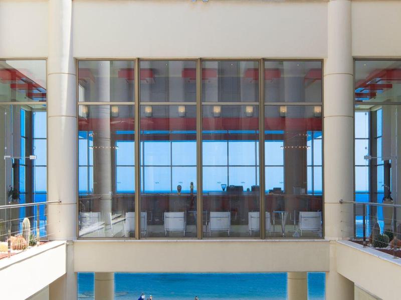 Vista di una terrazza di un hotel moderno con piscina, sedie a sdraio e vista sul mare.