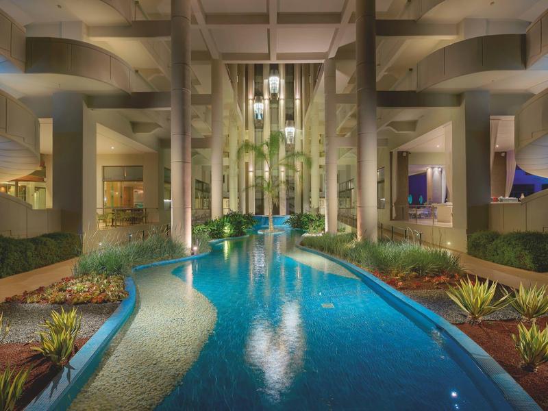 Piscina moderna illuminata in un hotel con piante e architettura contemporanea.