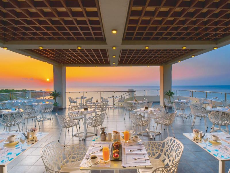 Area ristorante all'aperto con tavoli apparecchiati e vista sul tramonto sul mare.