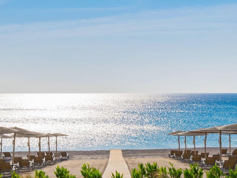 Spiaggia con lettini e ombrelloni davanti a un mare calmo e scintillante sotto un cielo blu