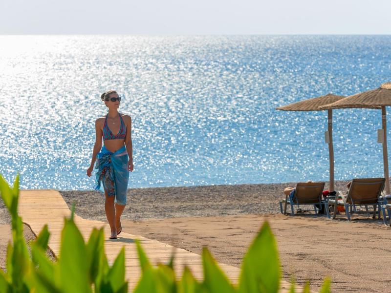 Donna che cammina su una spiaggia vicino al mare con ombrelloni e lettini.