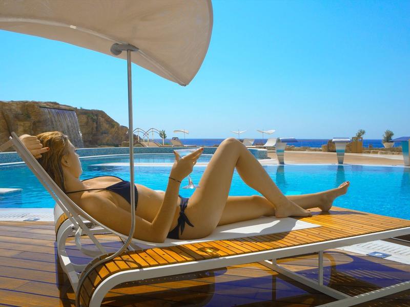 Donna rilassata su una sdraio accanto alla piscina con vista sul mare sotto un cielo azzurro.