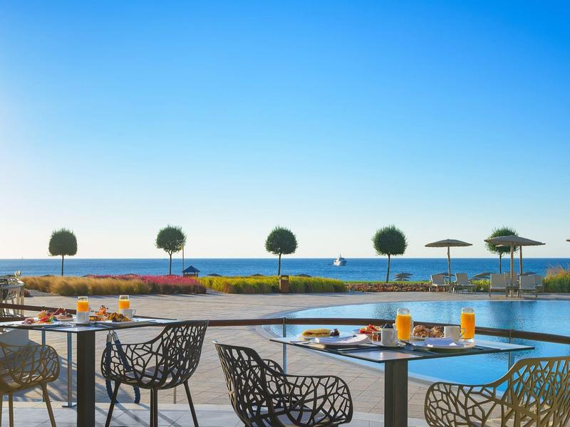 Terrazza con tavoli, sedie e piscina, vista sul mare sotto un cielo azzurro.