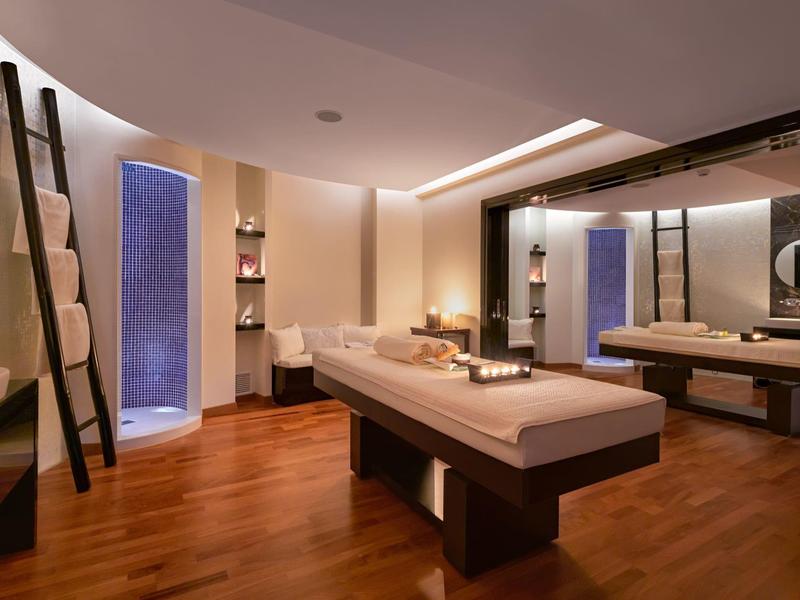 Sala massaggi elegante con tavolo centrale, pareti beige e pavimento in legno.