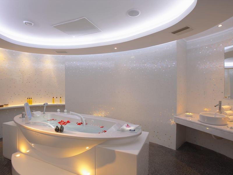 Bagno moderno con vasca idromassaggio rotonda, illuminazione soffusa e area lavabo riflettente.