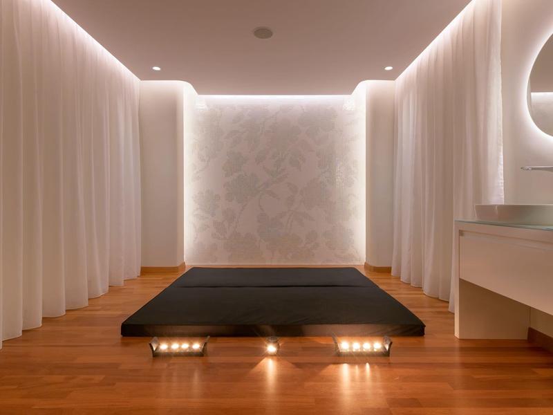 Camera d'hotel minimalista con letto basso e tende bianche che circondano la stanza.