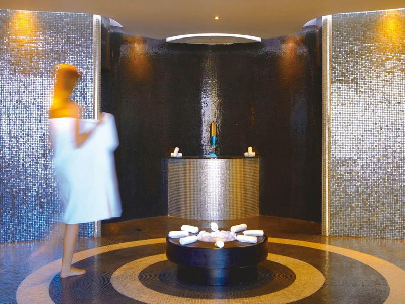 Ingresso elegante della spa con pareti scure, banco rotondo e illuminazione soffusa.