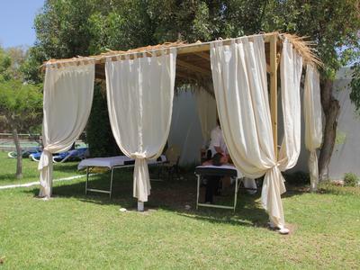 Area coperta con tende bianche e lettini su erba verde all'aperto.