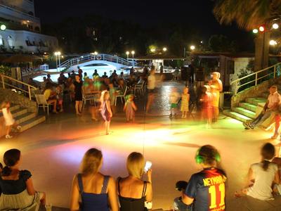 Noční osvětlená venkovní taneční plocha s lidmi sledujícími představení.