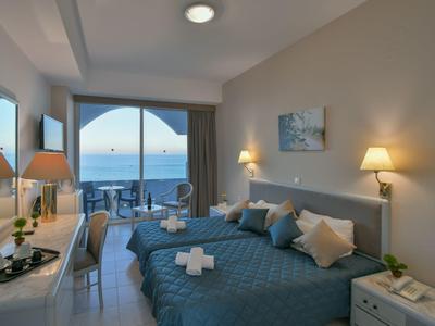 Camera d'hotel con balcone e vista mare, due letti e arredamento moderno.