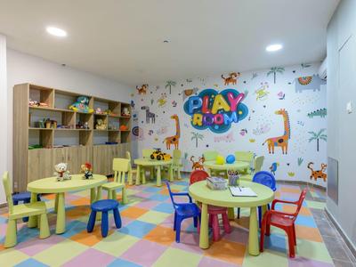Sala giochi colorata con tavoli, sedie e decorazioni murali con animali e scritta Play Room.