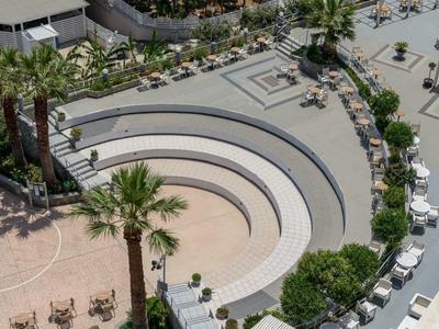 Anfiteatro all'aperto con gradini bianchi e palme in una zona alberghiera.