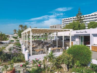 Area esterna dell'hotel con posti a sedere coperti e giardino verde sotto un cielo blu sereno.