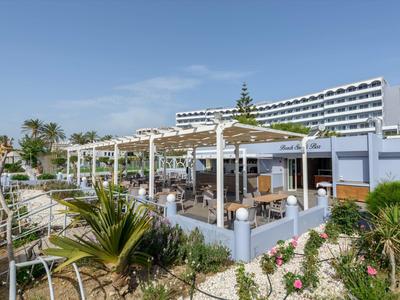 Hotelová terasa s pergolou, posezením a zahradními rostlinami pod jasnou oblohou