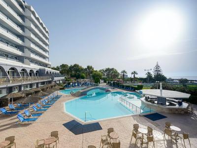 Moderní hotelový bazén s lehátky a výhledem na moře za jasné oblohy.