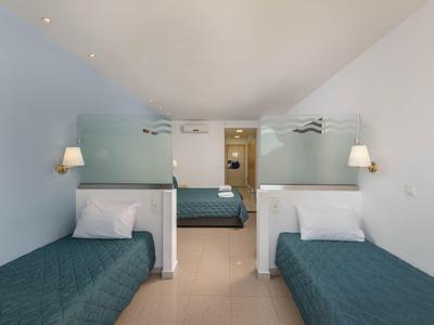 Camera d'hotel semplice con due letti singoli e un letto matrimoniale in un ambiente calmo e luminoso.