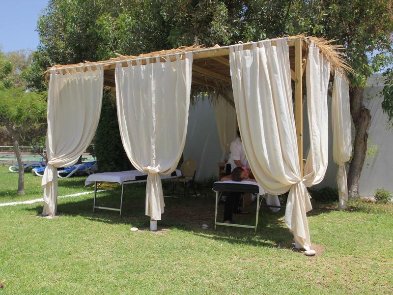 Area coperta con tende bianche e lettini su erba verde all'aperto.