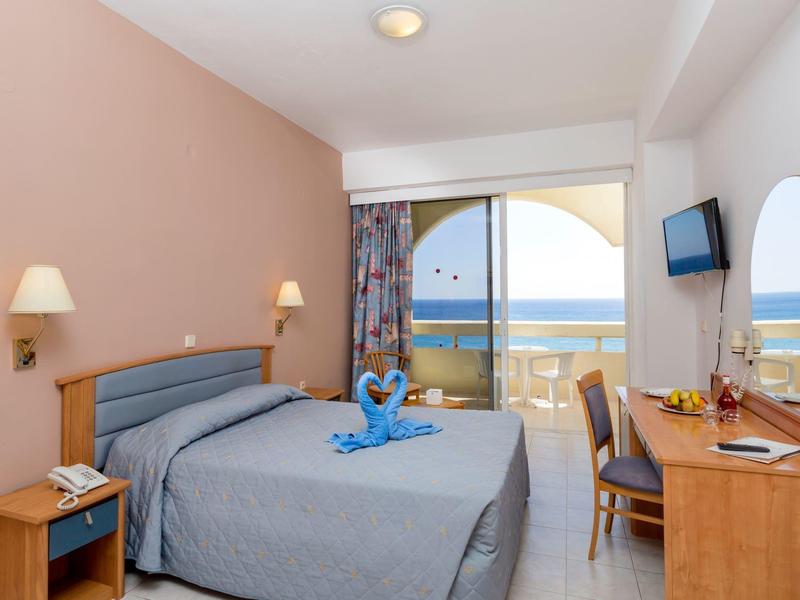 Camera d'hotel con letto matrimoniale, scrivania, balcone e vista mare.