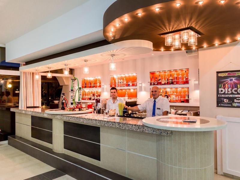 Bar dell'hotel moderno con illuminazione ambientale, due baristi e design elegante.