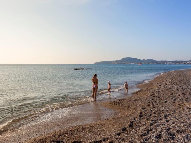 Persone che si godono una camminata tranquilla sulla spiaggia sotto un cielo limpido e mare calmo.