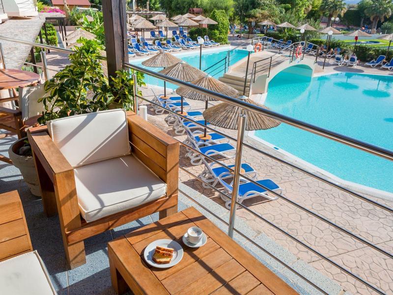 Vista da una terrazza con sedia e tavolo su una piscina con lettini blu.