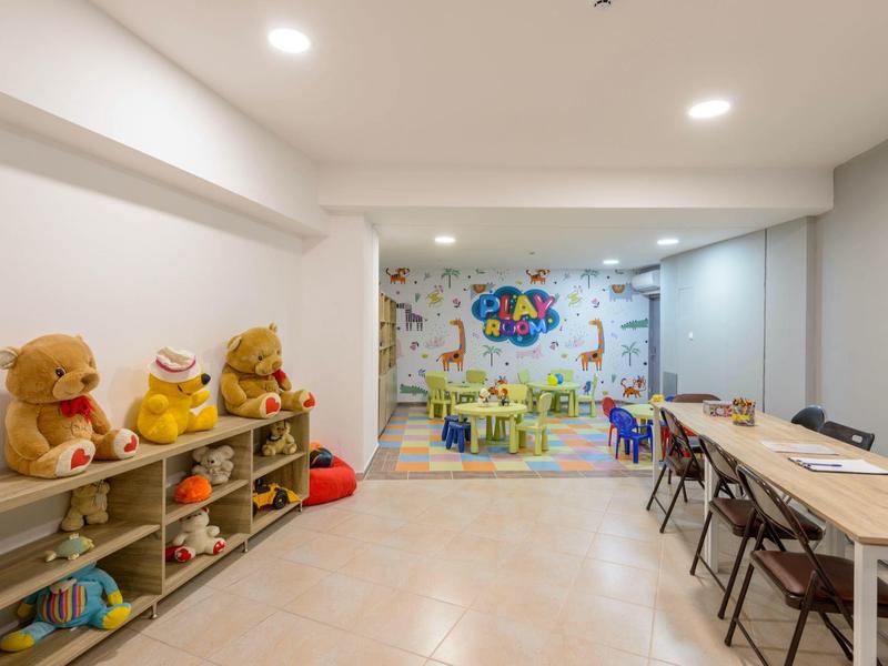 Stanza per bambini con scaffali per giocattoli, murale colorata e tavoli con sedie.