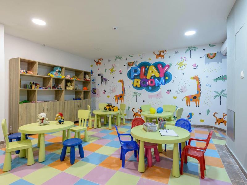 Sala giochi colorata con tavoli, sedie e decorazioni murali con animali e scritta Play Room.
