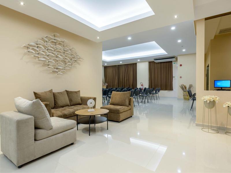 Lounge d'hotel moderna con pareti beige, poltrone comode e illuminazione indiretta sul soffitto.