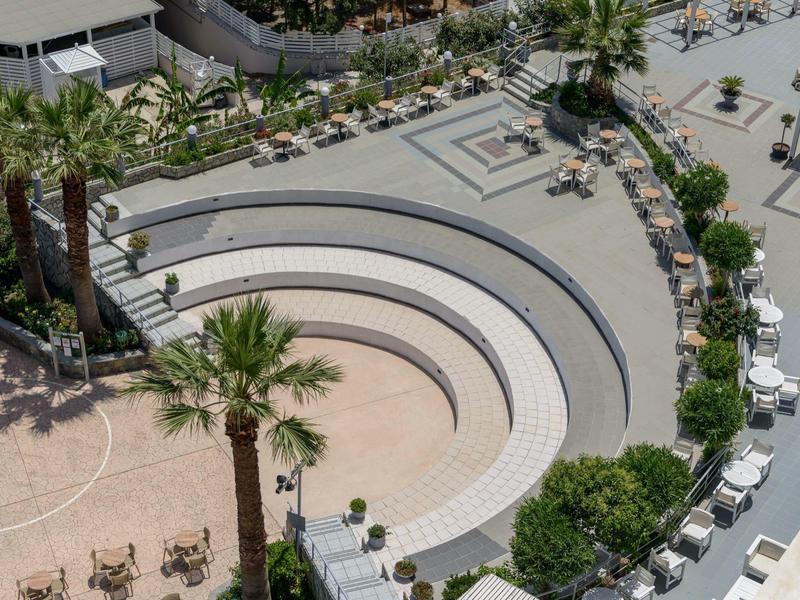 Anfiteatro all'aperto con gradini bianchi e palme in una zona alberghiera.