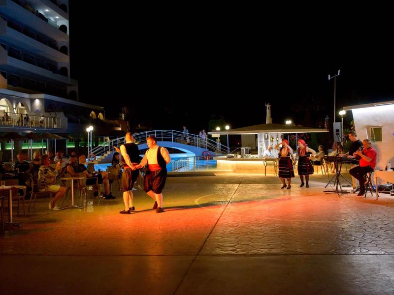 Piazza illuminata con persone che camminano e siedono in un'area dell'hotel di notte.