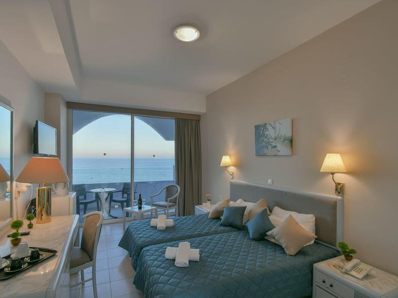 Camera d'albergo luminosa con letto matrimoniale, balcone e vista mare al tramonto.