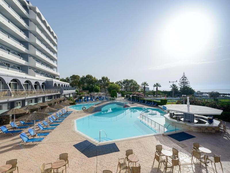 Area piscina di un hotel con lettini, tavoli e vista mare sotto un cielo limpido.