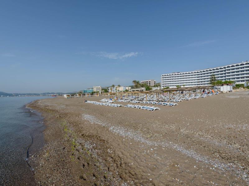 Spiaggia con lettini e ombrelloni accanto a un grande hotel sul mare.