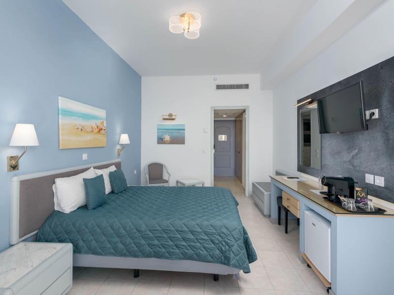 Camera d'hotel moderna con grande letto matrimoniale, scrivania, sedia e TV a schermo piatto a parete.