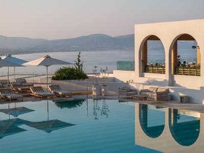 Spokojna strefa basenowa z leżakami, parasolami i widokiem na morze i góry w tle.