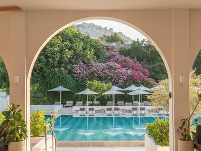 Widok przez łuk na basen z leżakami i parasolami w hotelowym ogrodzie.