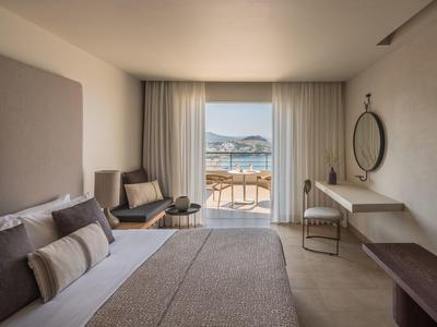 Moderne hotelkamer met royaal bed, zithoek en uitzicht op terras en zee