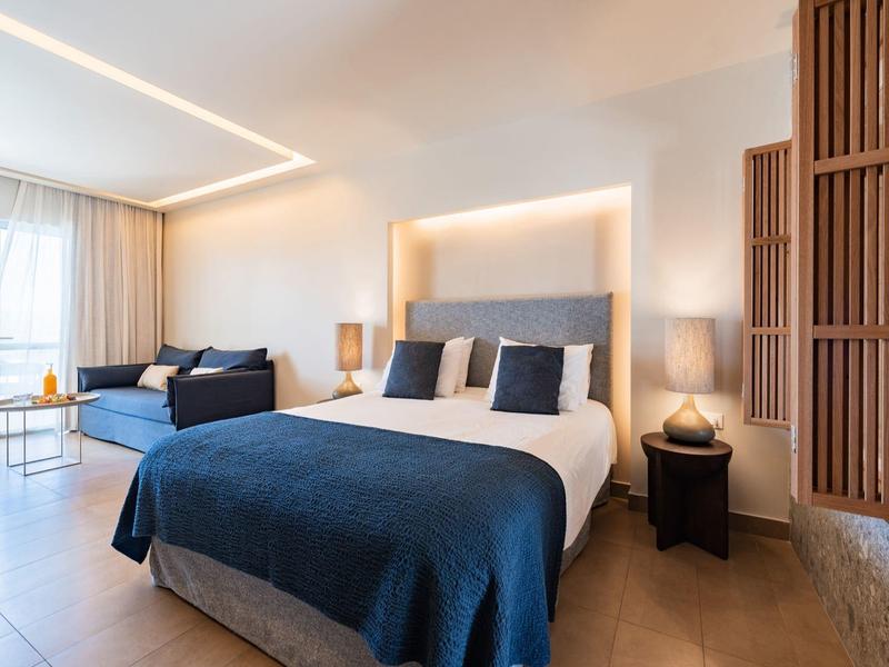 Moderne hotelkamer met een groot bed, blauwe accenten, bank en natuurlijk licht.