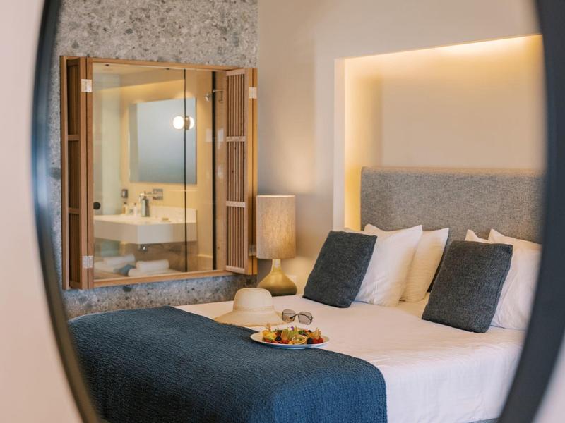 Gezellige hotelkamer met bed, kussens, nachtlampje en badkamerreflectie in spiegel.