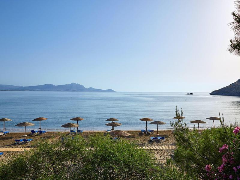 Rustig strand met parasols, ligstoelen en helderblauwe zee onder een zonnige hemel.