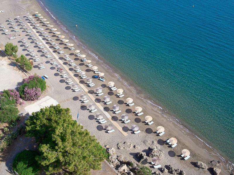Een strand met rijen witte parasols en ligstoelen naast een kalme blauwe zee.