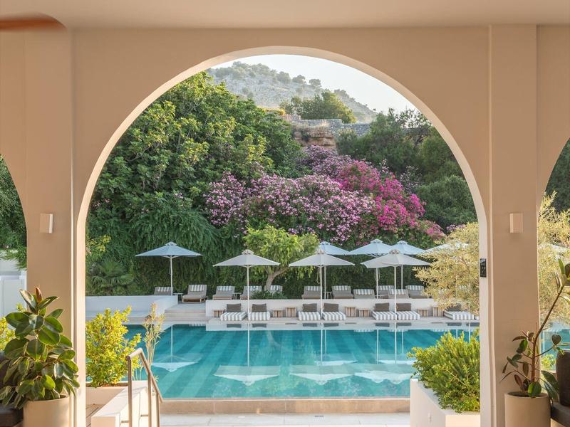 Hotelzwembad met witte ligstoelen en planten, uitzicht door een witte boog.
