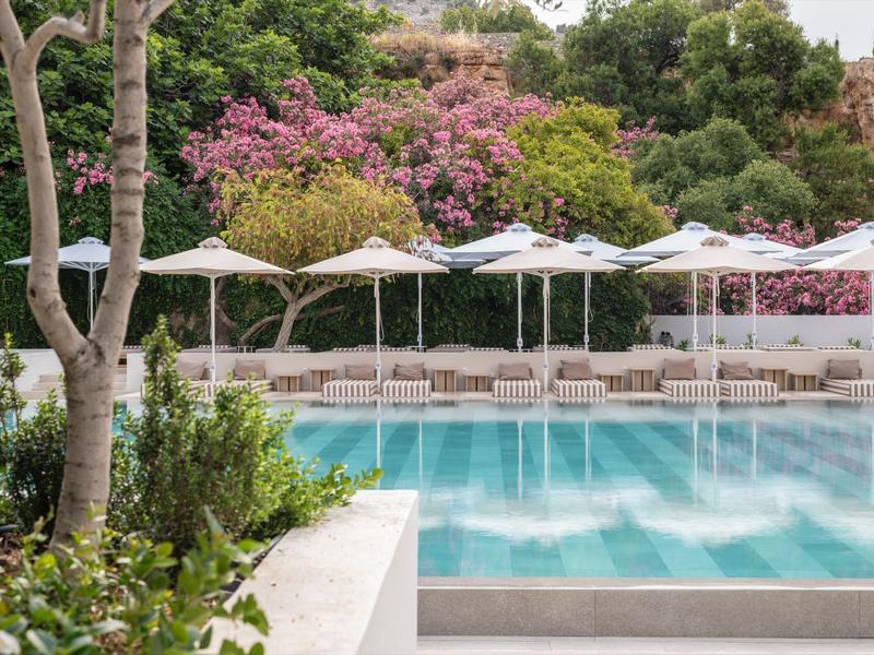 Een buitenzwembad met ligstoelen en witte parasols, omgeven door bloeiende bomen.