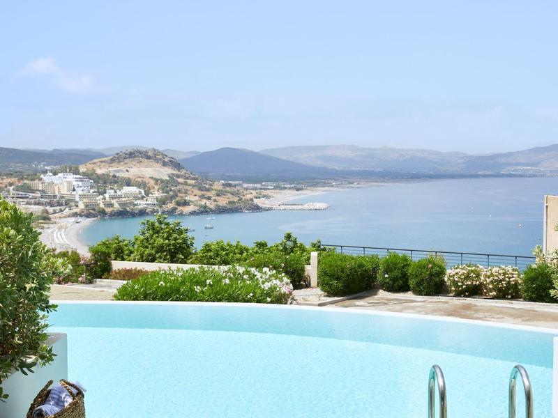 Buitenzwembad met ligstoelen en uitzicht op zee aan de kust onder een heldere hemel.