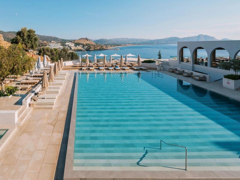 Luxe buitenzwembad met ligbedden met uitzicht op zee en heuvels.