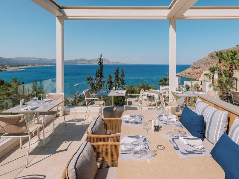 Buitenrestaurantterras met uitzicht op zee, tafels gedekt voor diner onder een pergola.