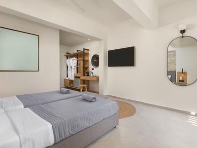 Helles Schlafzimmer mit grauem Bett, Wandspiegel, TV und offenem Kleiderschrank.