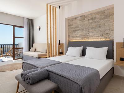 Modernes Schlafzimmer mit Doppelbett, grauen Decken, hellen Wänden und Balkon mit Meerblick.