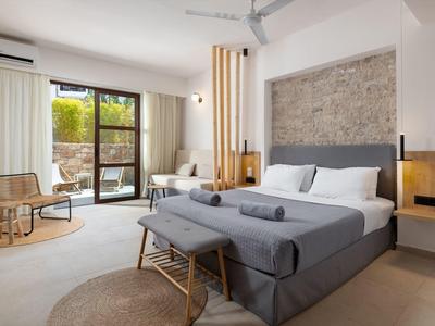Modernes Schlafzimmer mit großem Bett, grauer Bettwäsche, Holzstuhl und Zugang zum Balkon.